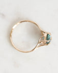 A delicate gold ring with a curved, openwork band and a small oval green gemstone, resting on a light marble surface.