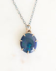 Dark colored opal set in gold with an oxidized chain against a plain background. 