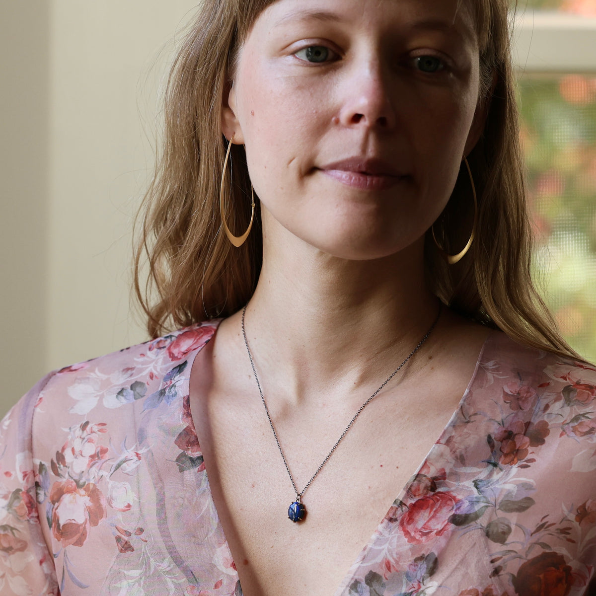 Woman wearing opal necklace and floral blouse photographed against an indoor background.