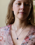Woman wearing opal necklace and floral blouse photographed against an indoor background.