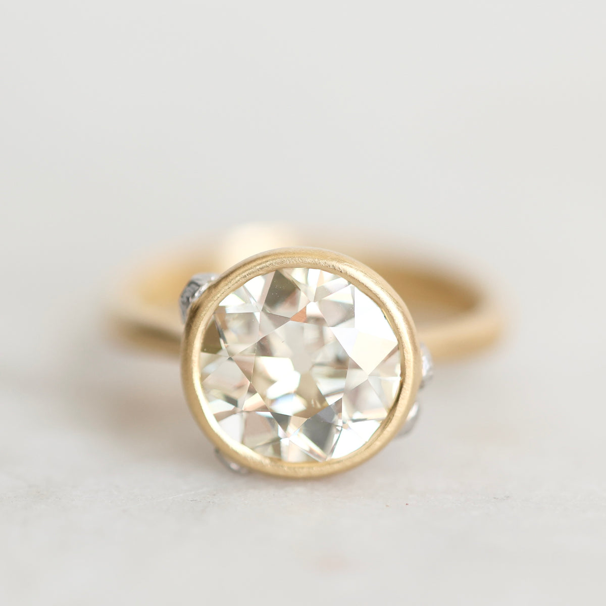 A gold ring with a large round-cut clear gemstone in a bezel setting, photographed on a light neutral background.