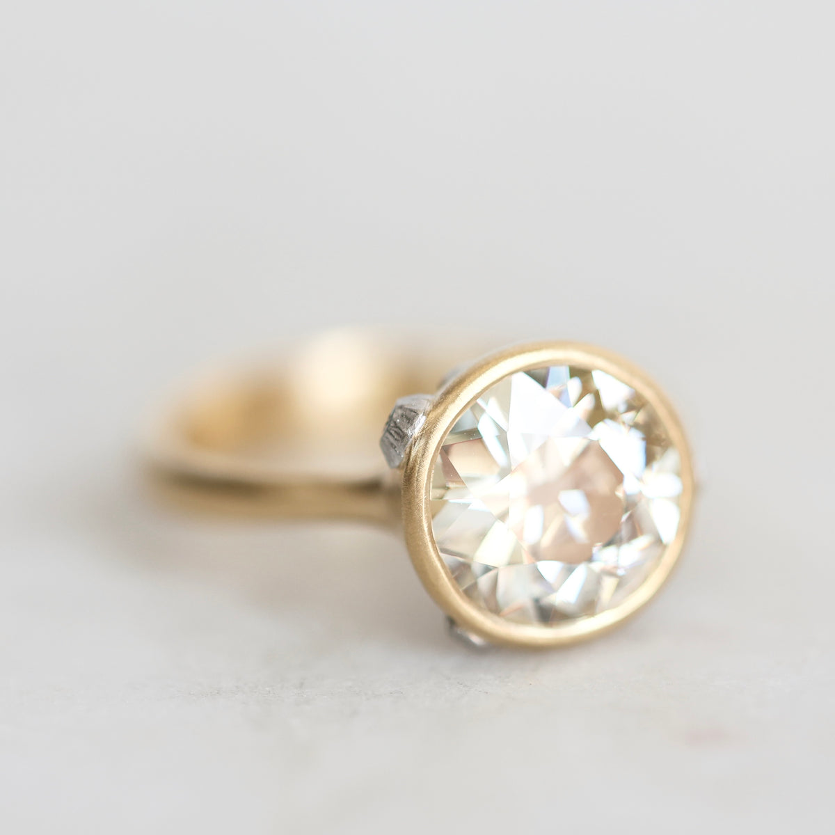Gold bezel set diamond ring with platinum barnacle accent photographed against a white background. 