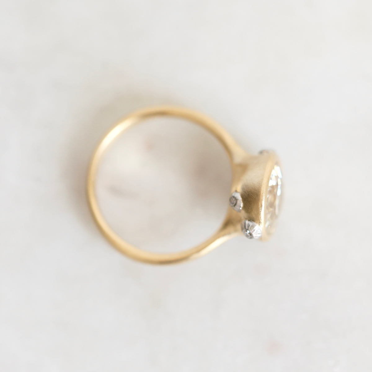 A gold ring with a small cluster of clear gemstones on a light, off-white textured surface.