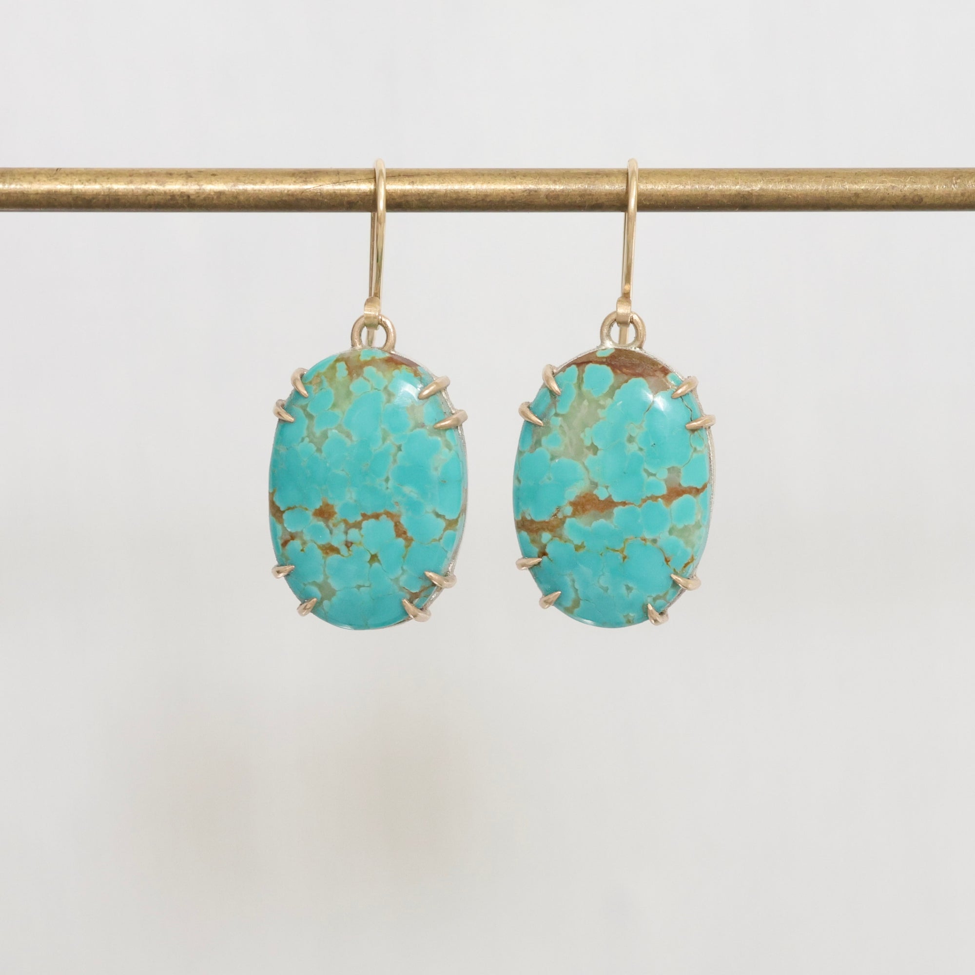 Turquoise stone earrings on a gold earring stand against a white background