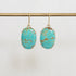 Turquoise stone earrings on a gold earring stand against a white background