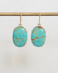 Turquoise stone earrings on a gold earring stand against a white background