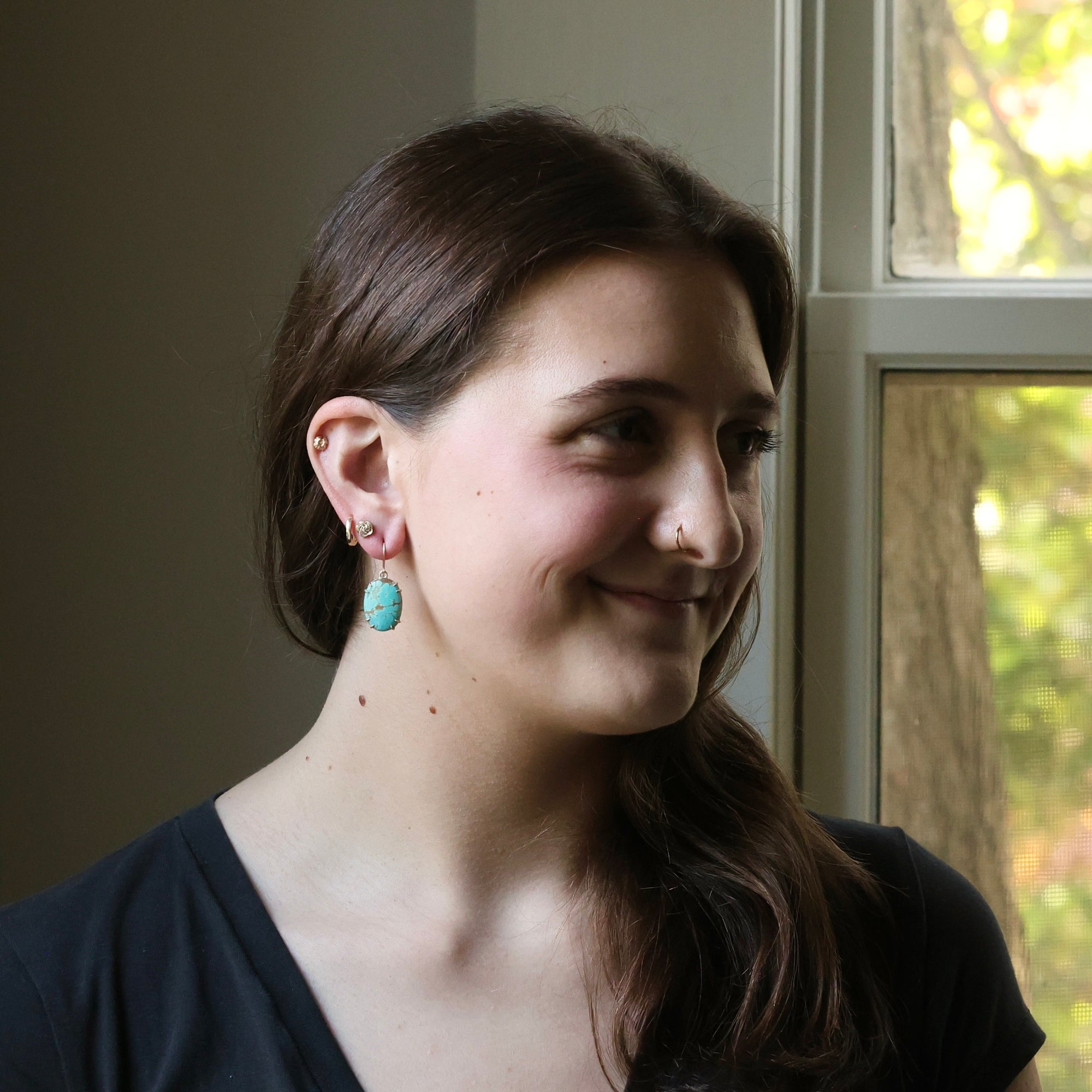 Woman with earrings and a nose ring smiling in front of a window