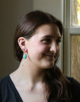 Woman with earrings and a nose ring smiling in front of a window