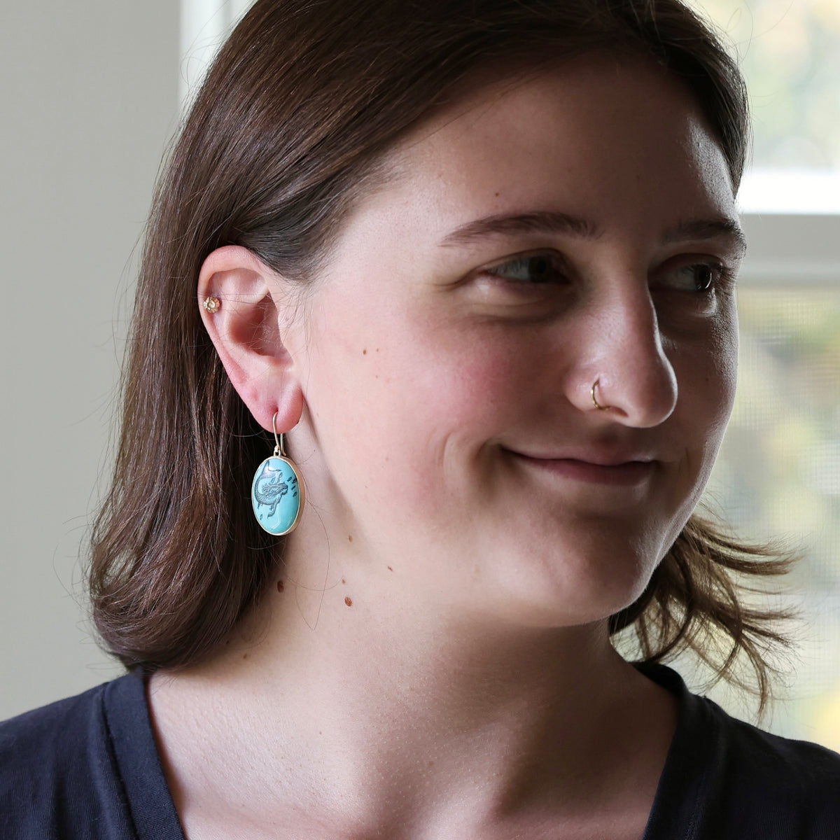Woman wearing large turquoise earring with engraved mermaid.
