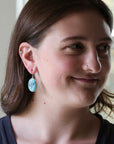 Woman wearing large turquoise earring with engraved mermaid.