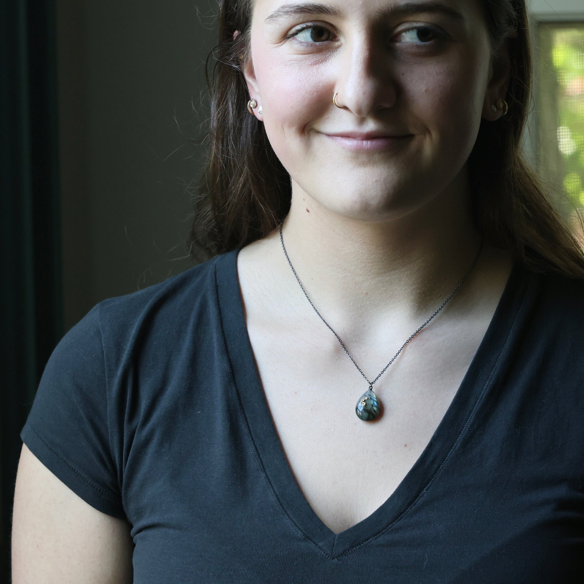 Woman wearing a dark gray shirt with a necklace, indoors.