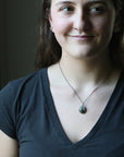 Woman wearing a dark gray shirt with a necklace, indoors.