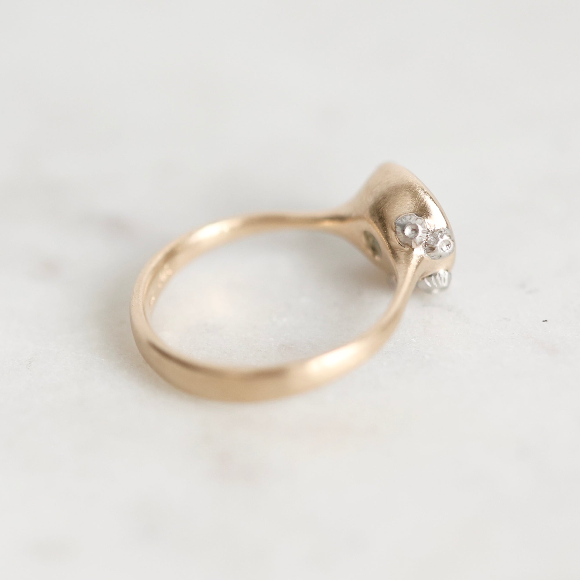 A close-up of a gold ring with a small cluster of clear gemstones on the setting, photographed on a light marble surface.