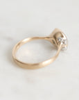 A close-up of a gold ring with a small cluster of clear gemstones on the setting, photographed on a light marble surface.