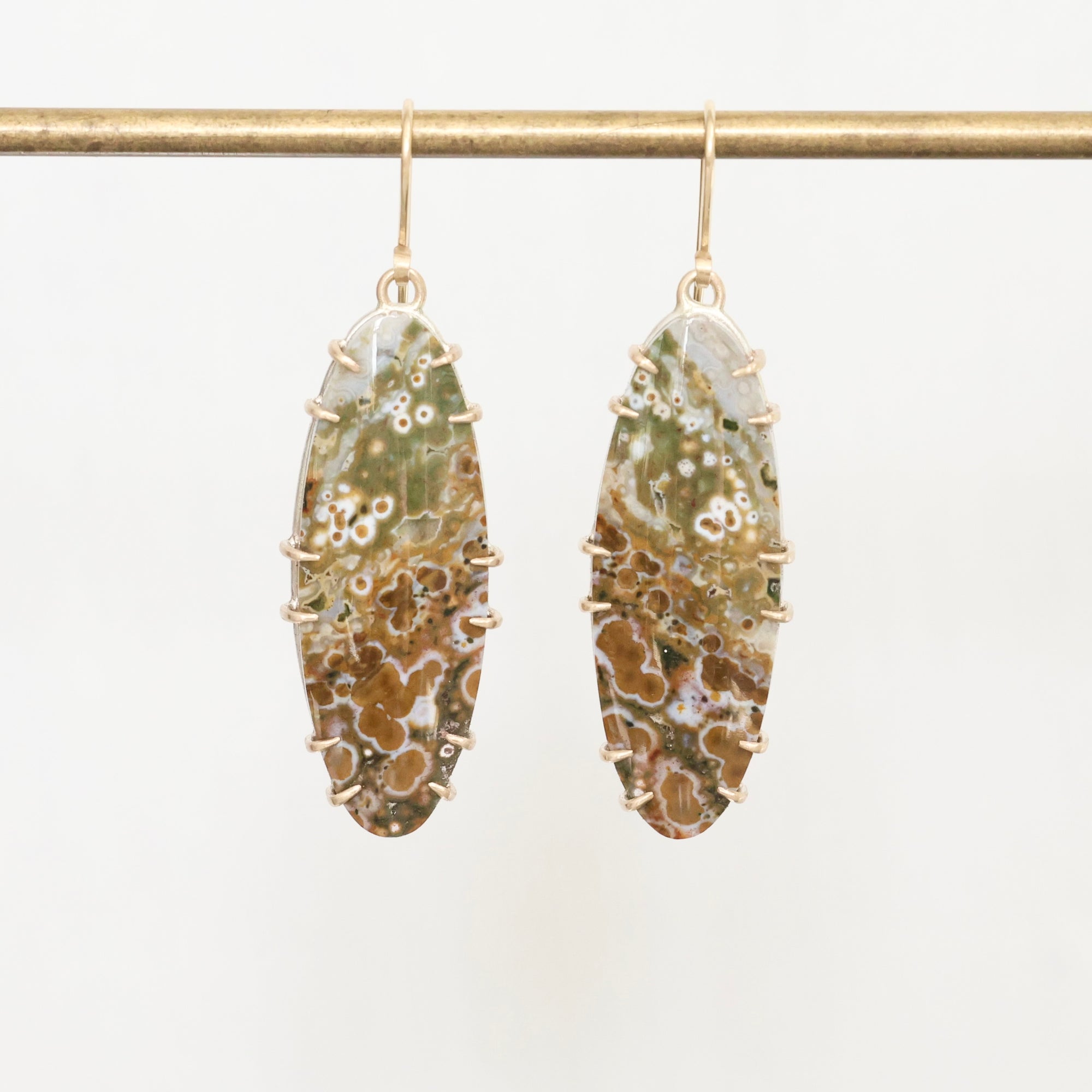 Pair of earrings with marbled green and brown stones on a white background