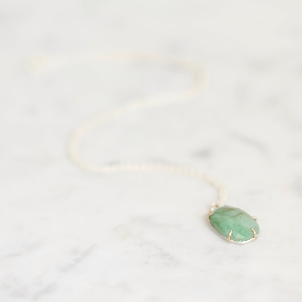 A delicate gold chain necklace with a green gemstone pendant, resting on a light gray marble surface.