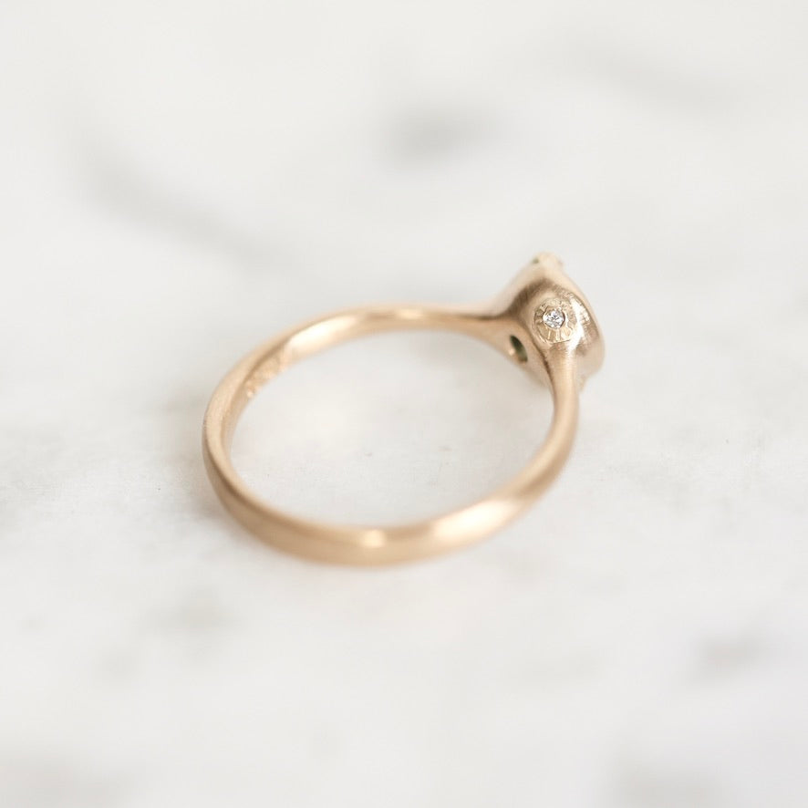 A close-up of a rose gold ring with a small clear gemstone on a light marble surface.