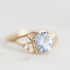 A gold ring featuring a large oval light blue gemstone in a prong setting, with small round accent stones along the band, photographed on a soft light gray background.