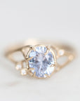 A delicate gold ring featuring a large oval-cut light blue gemstone in a prong setting, accented by two small round clear stones on the shoulders, photographed on a soft white background.