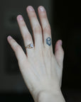 A close-up of a person's hand wearing a delicate gold ring with a small clear gemstone, set against a dark, blurred background.