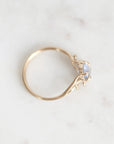 A delicate gold ring with a small light blue gemstone, photographed on a light marble surface.