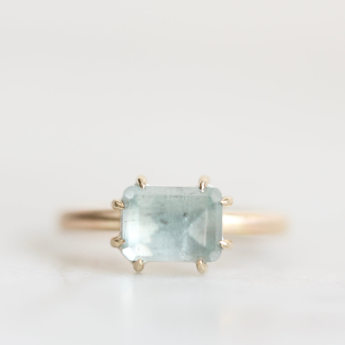 A gold ring featuring a rectangular light blue gemstone in a prong setting, photographed against a clean white background.