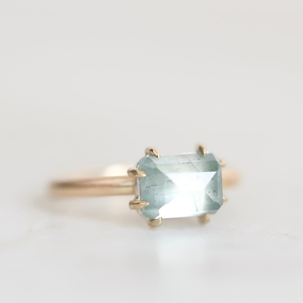 A gold ring featuring a rectangular light blue gemstone in a prong setting, photographed against a clean white background.