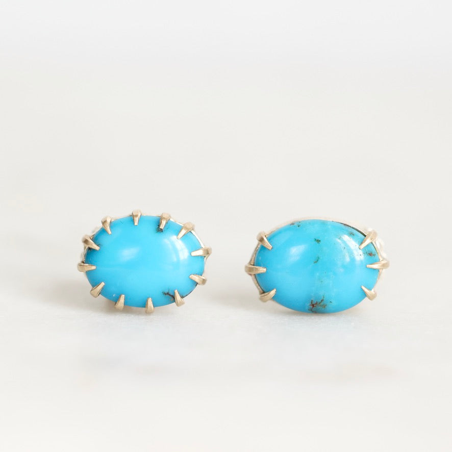 A pair of oval turquoise stud earrings with gold prong settings, displayed on a clean white surface.