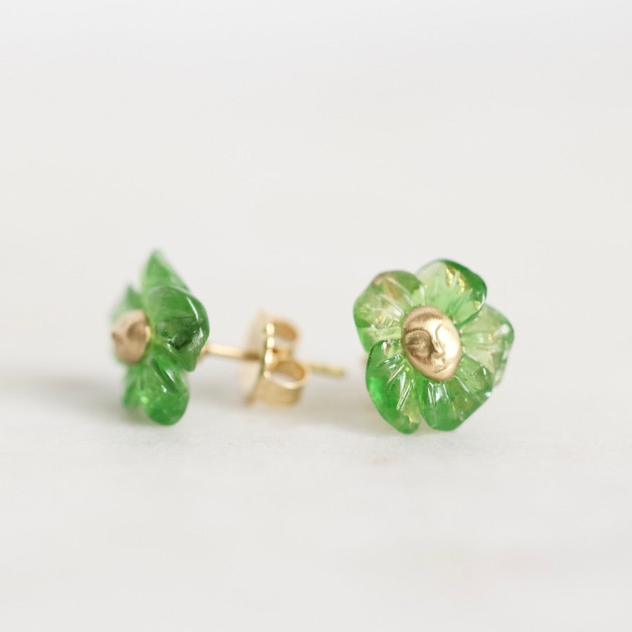 A pair of small flower-shaped stud earrings with translucent green petals and gold-tone centers, shown on a plain light background.
