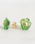 A pair of small flower-shaped stud earrings with translucent green petals and gold-tone centers, shown on a plain light background.