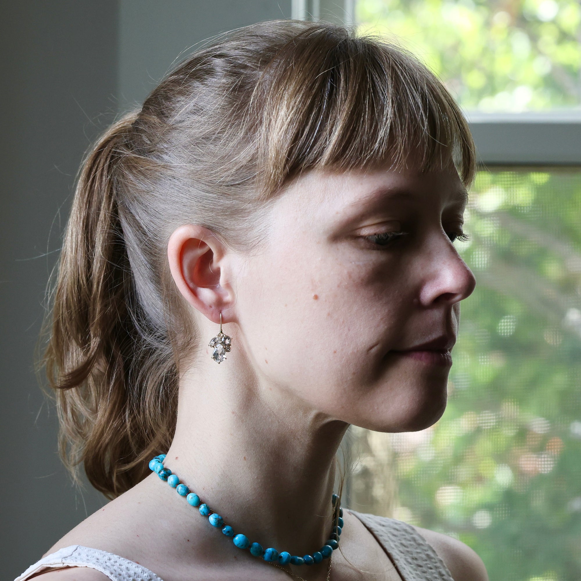 Woman wearing a blue necklace with a blurred outdoor background