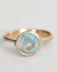 Gold ring with a light blue gemstone on a light gray background