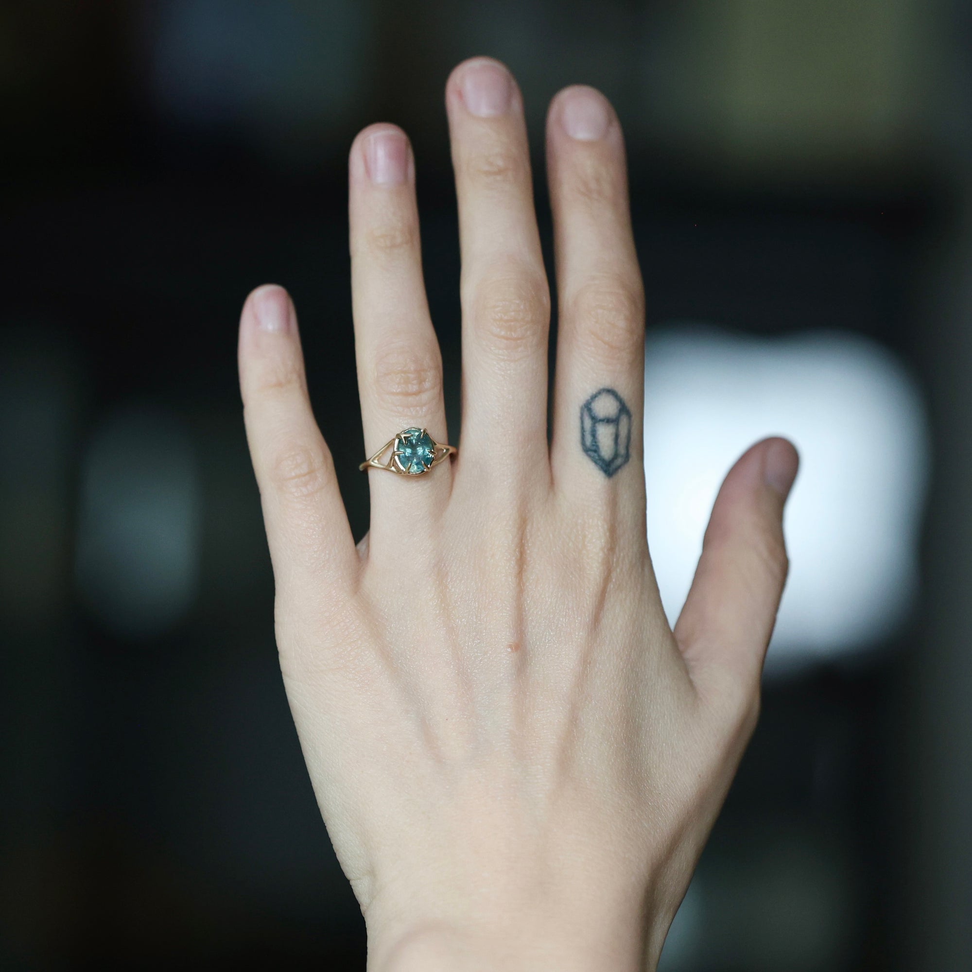 Large stone ring with branchy prongs on hand with tattoo