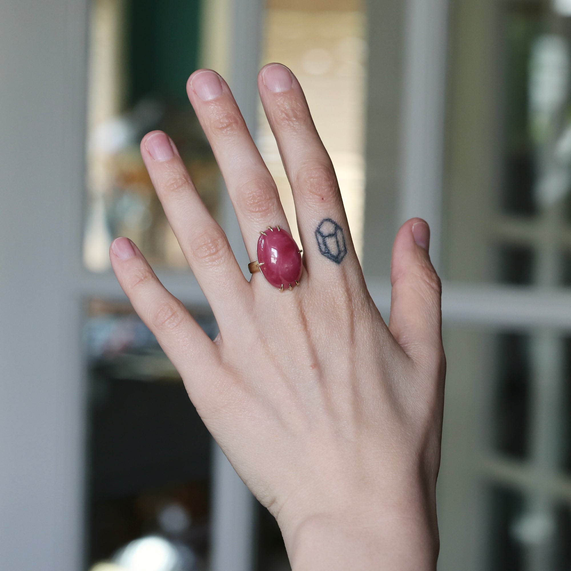 Hand with a red ring and tattoo on a blurred indoor background