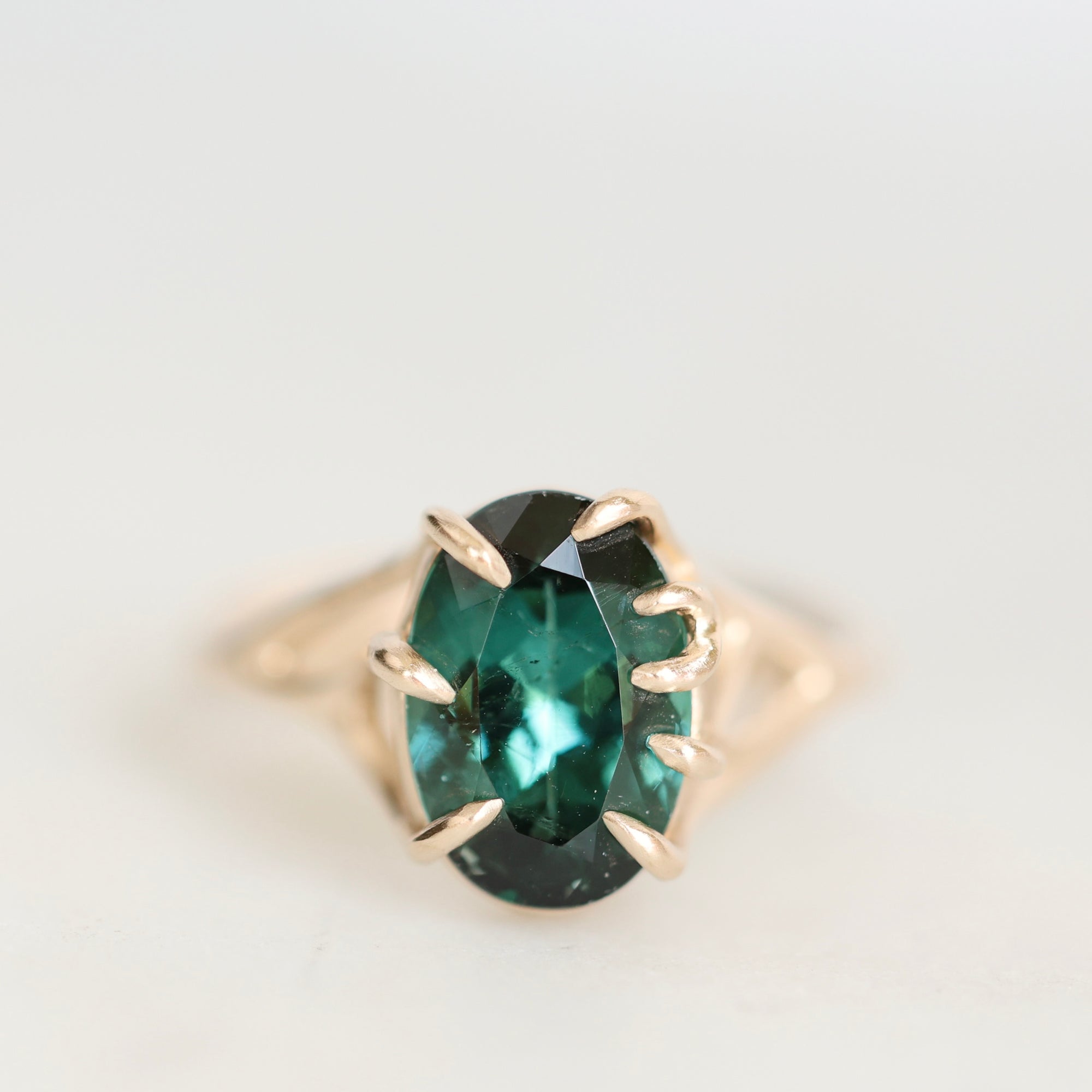 An oval-cut emerald-cut green gemstone ring set in a gold prong setting, shown on a clean white background.