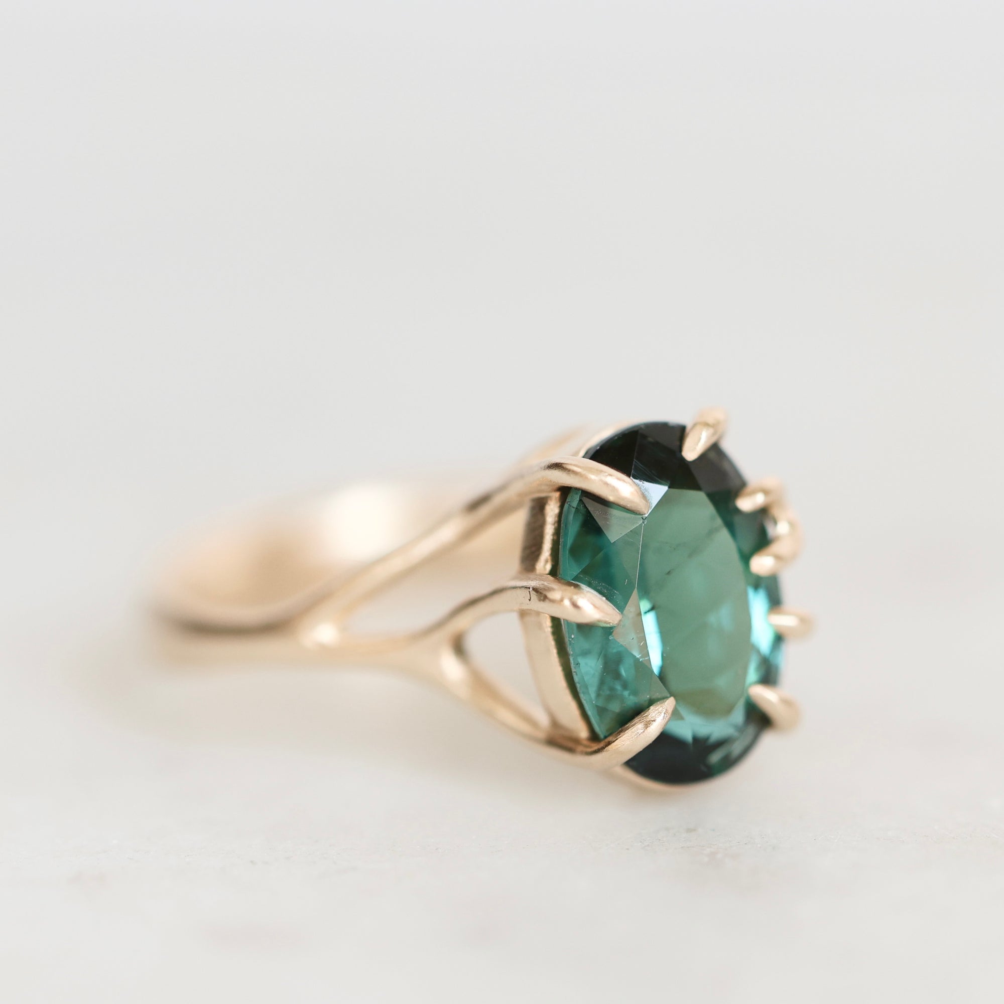 A gold ring with a faceted green gemstone, photographed on a clean, light gray background.