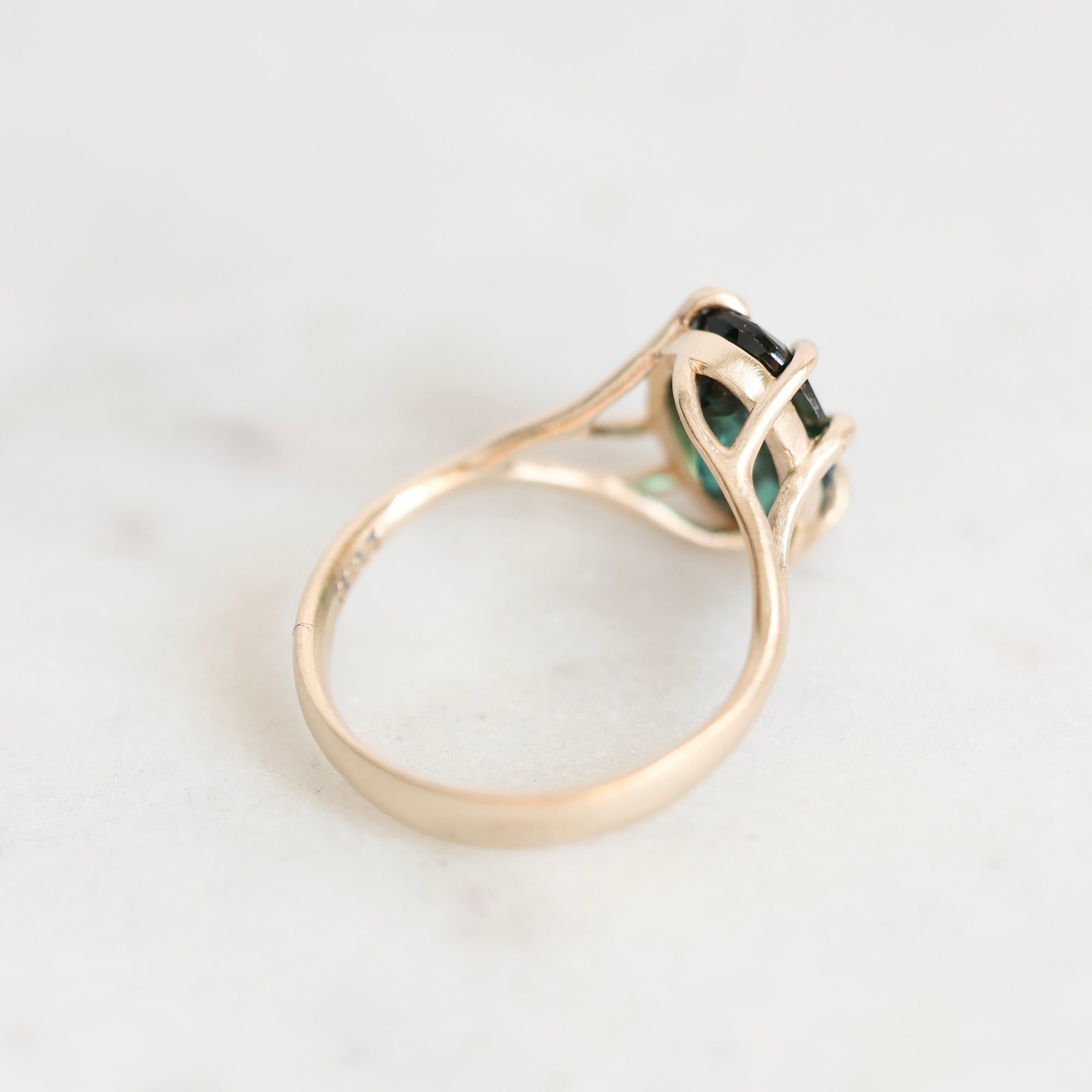 A gold ring with a green gemstone, photographed on a light marble surface.