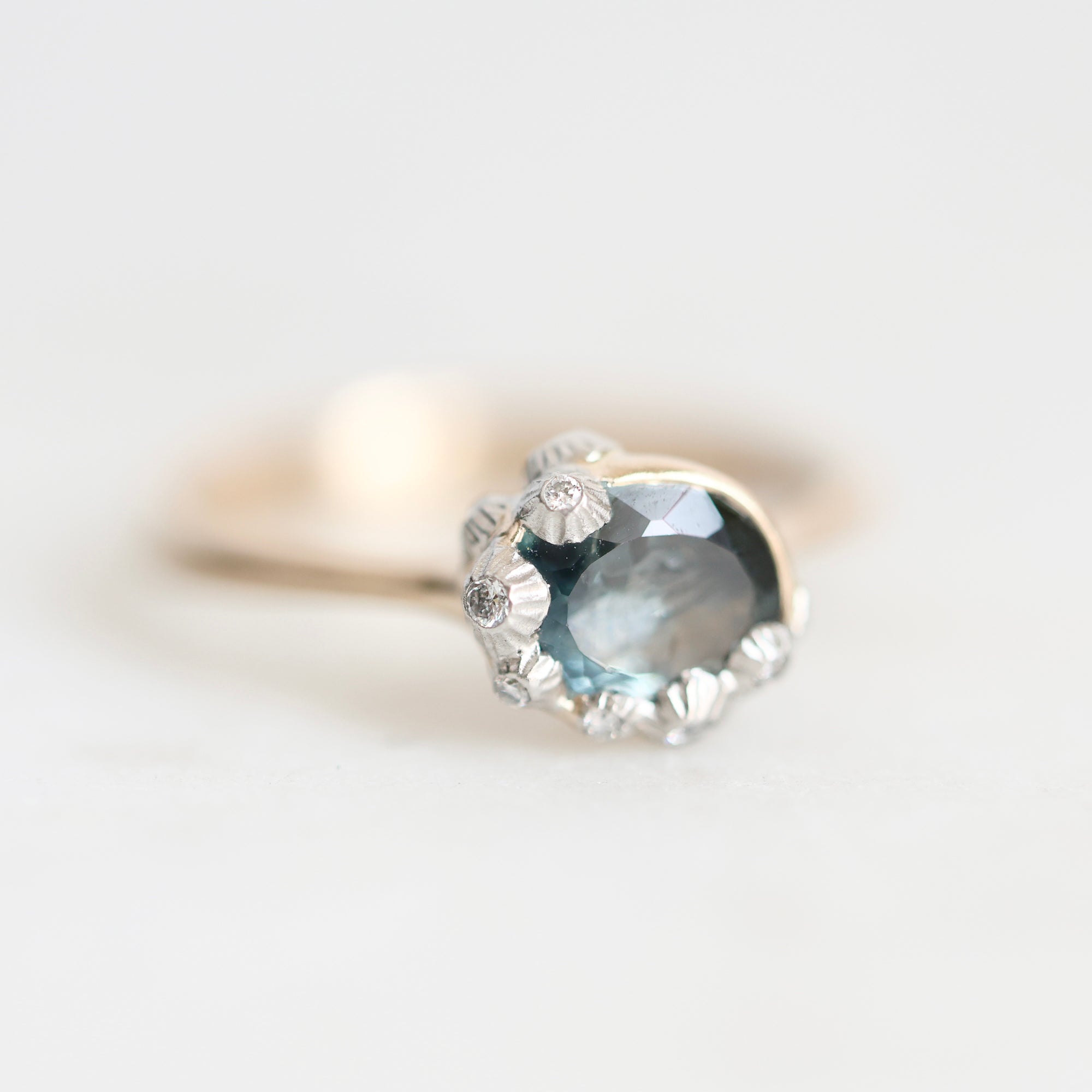 A gold ring featuring a large oval light blue gemstone surrounded by small silver flower-like accents, photographed on a soft white background.