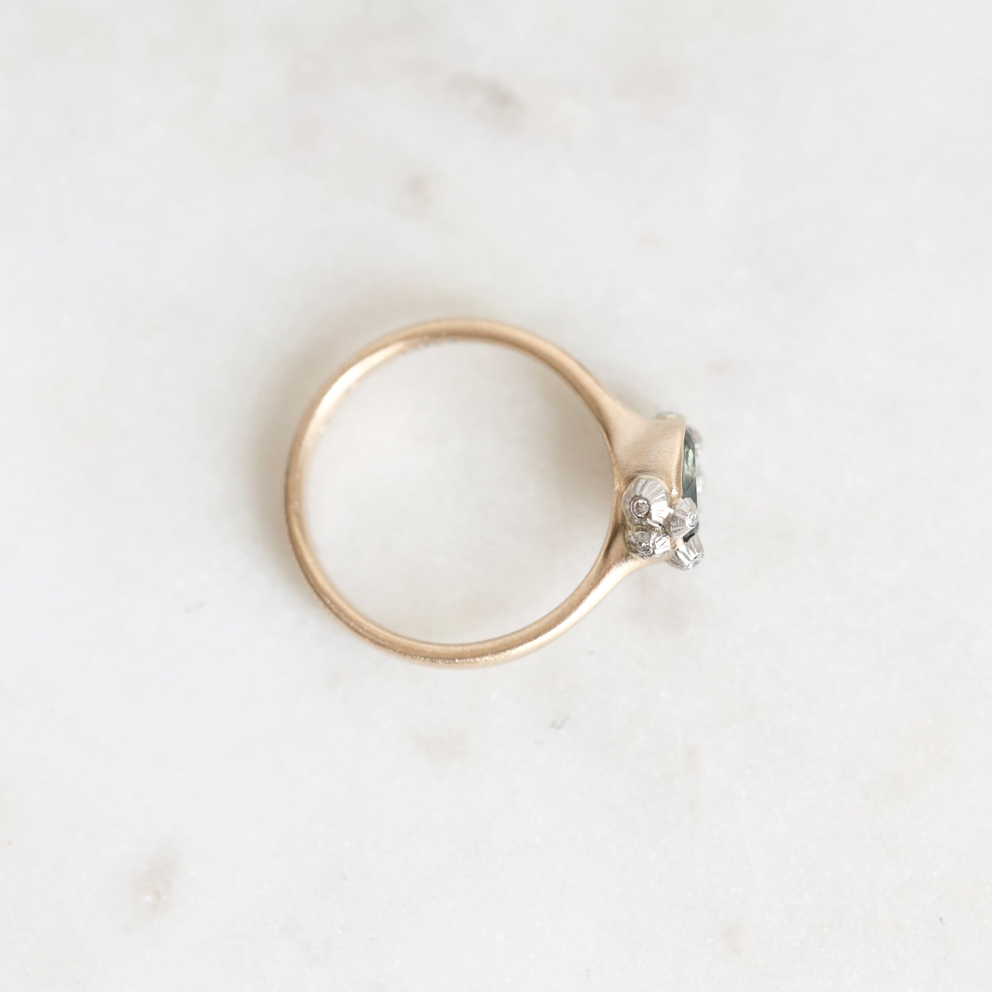 A gold ring with a small clear gemstone in a prong setting, photographed on a light marble surface.