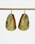 A pair of organic-shaped dangle earrings made from polished green and brown stone, hanging from gold fishhook wires against a plain white background.