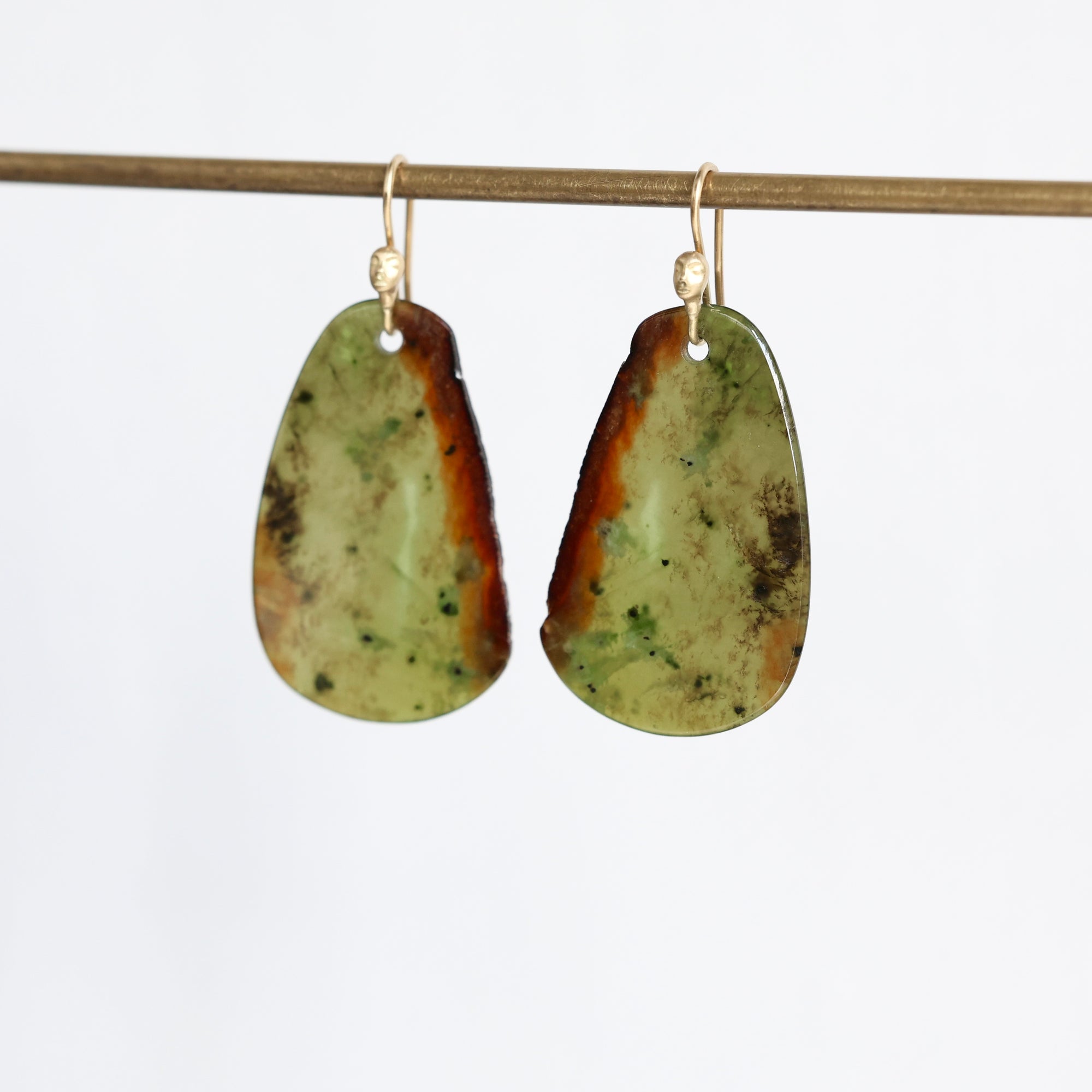 A pair of organic-shaped teardrop earrings made from natural green and brown jasper stone, hanging from gold fishhook wires against a plain white background.