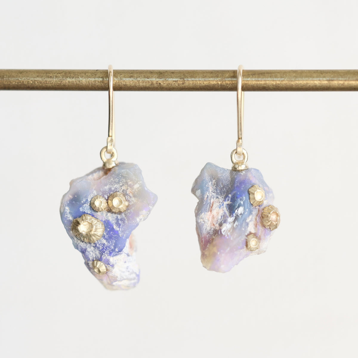 Fossilized opal drop earrings with gold barnacle details against a white background. 