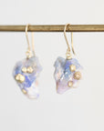 A pair of dangle earrings featuring iridescent blue and white fossilized opal with small gold metallic accents, hanging from gold-toned French hook wires on a gold-colored horizontal rod against a light gray background.