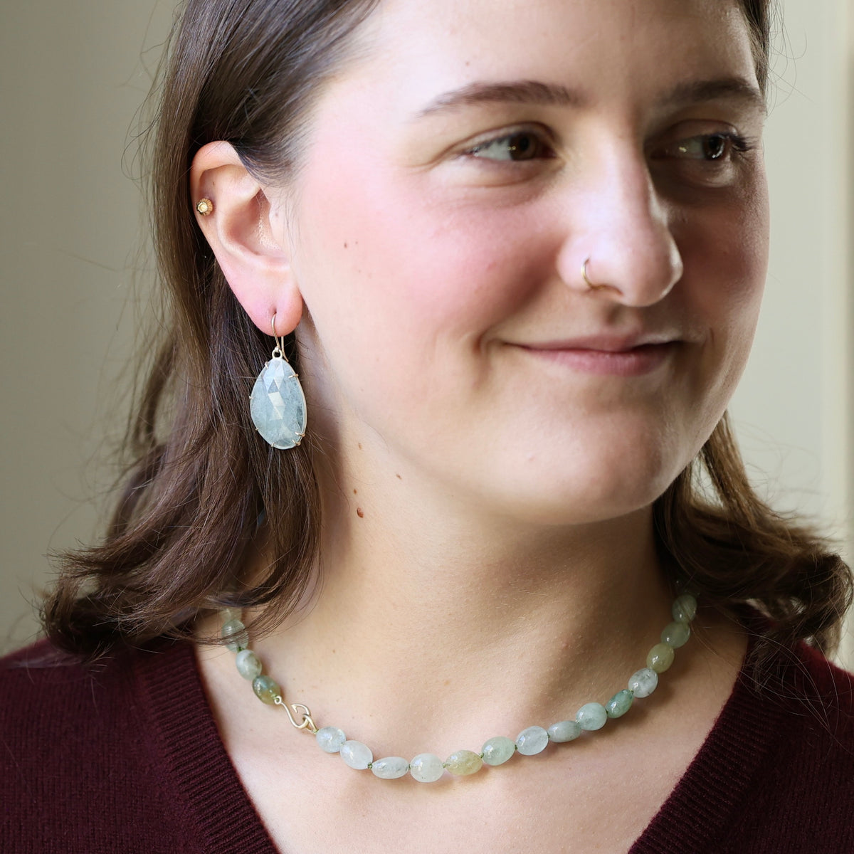 A woman wearing a light blue-green beaded necklace and matching teardrop earrings with gold-toned settings, shown in a close-up portrait.