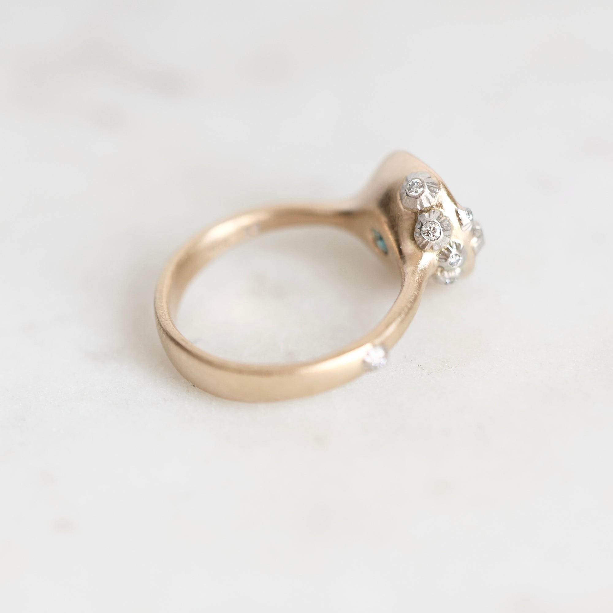 A gold ring with a cluster of small clear gemstones on the setting, photographed on a light marble-like surface.