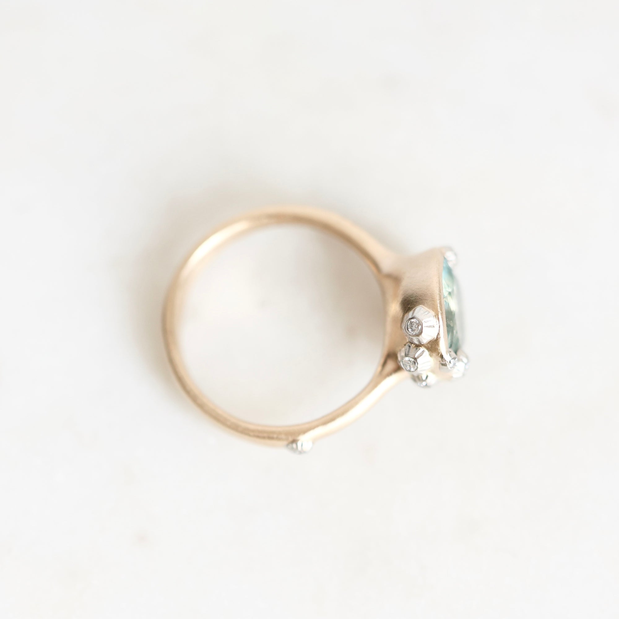 A gold ring with a small cluster of clear gemstones on the side, photographed on a plain white background.