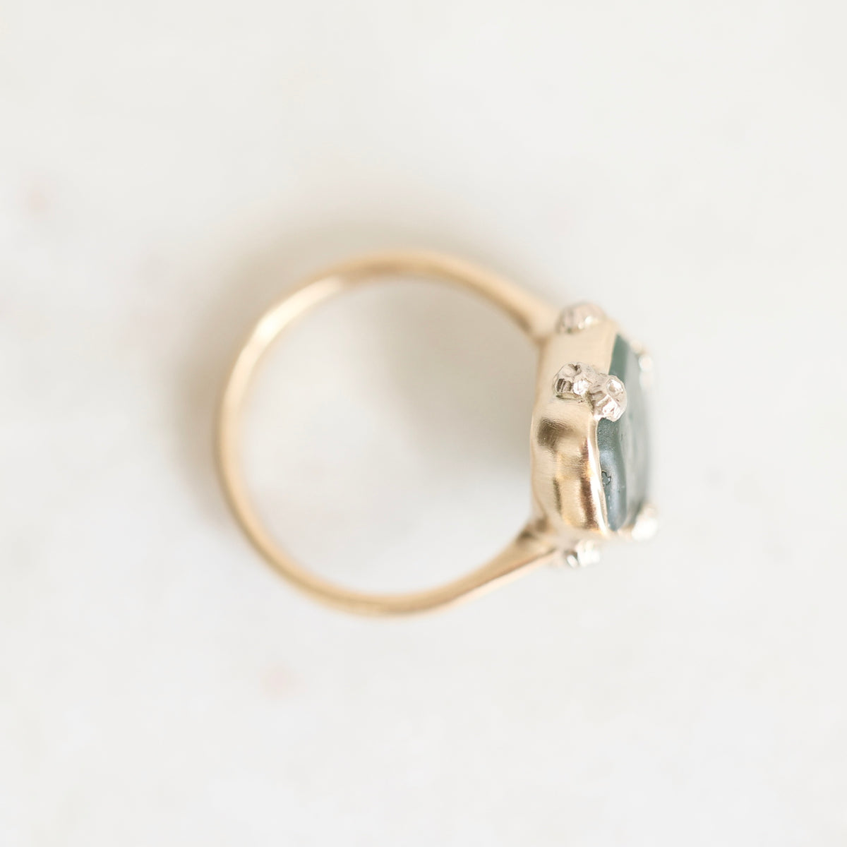 A gold ring with a small cluster of clear stones and a pale blue-green rectangular gemstone, photographed on a plain light background.