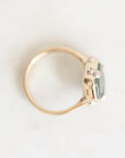 A gold ring with a small cluster of clear stones and a pale blue-green rectangular gemstone, photographed on a plain light background.
