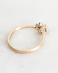 A close-up shot of a gold ring with a textured band and a cluster of small clear gemstones on the setting, resting on a light marble surface.