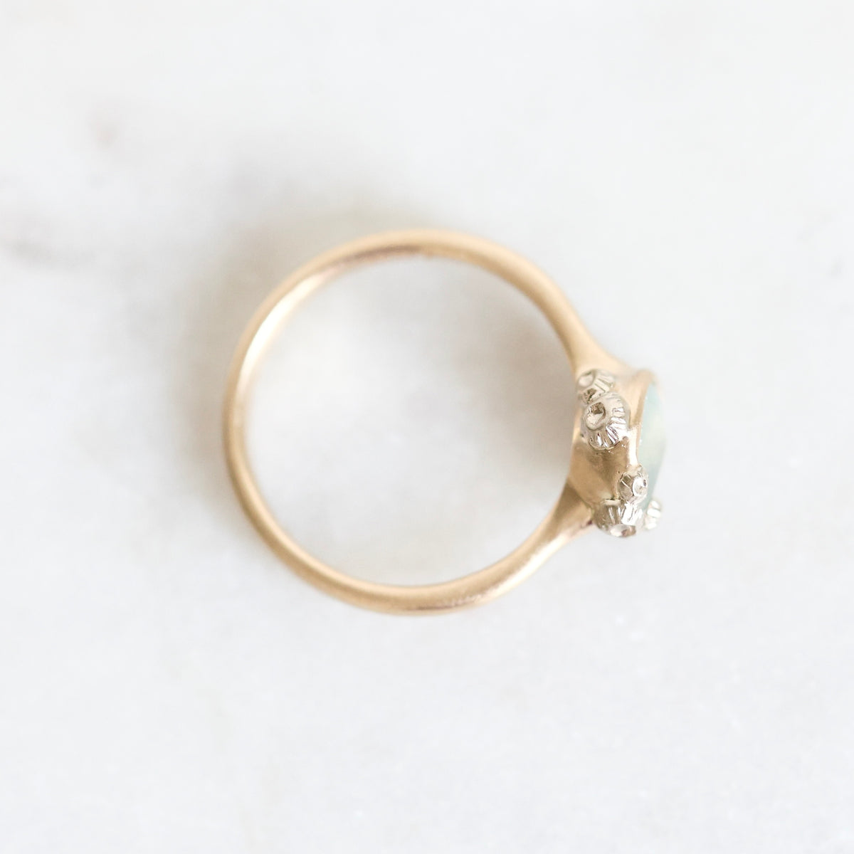 A gold ring with a small cluster of clear gemstones on a light, textured white background.